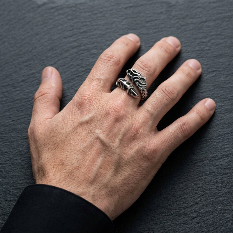 Dragon armor sterling silver bypass ring on a man's middle finger, with a relaxed full hand and black shirt cuff against charcoal stone