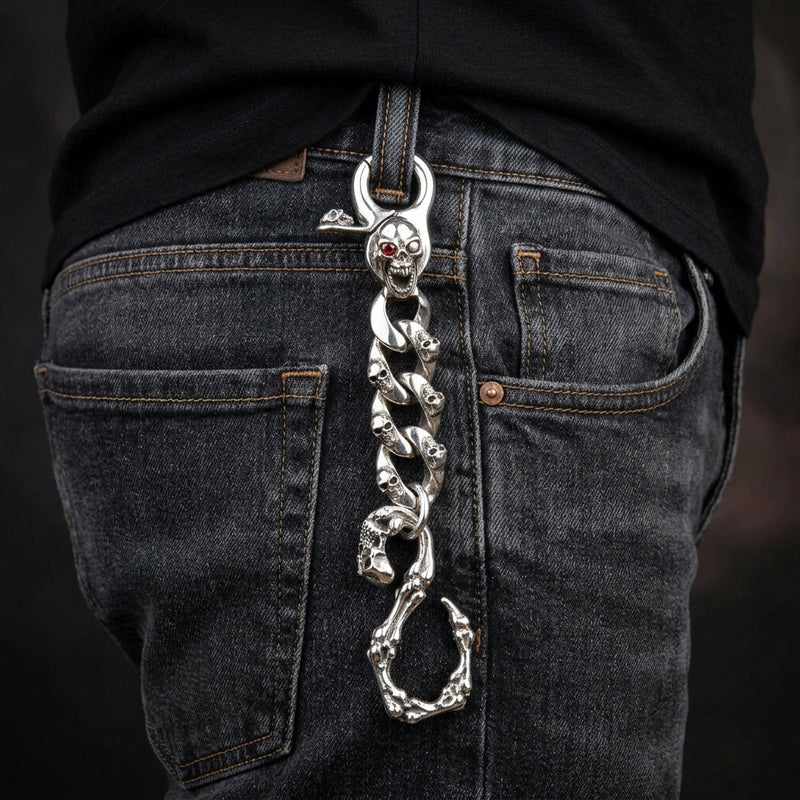 Sleutelhanger van sterling zilver met doodshoofd met rood oog, hangend aan de riemlus van een donkere denim jeans.