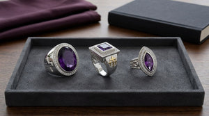 Oval, square and marquise amethyst silver rings with cross and crozier shoulder details on a dark tray.
