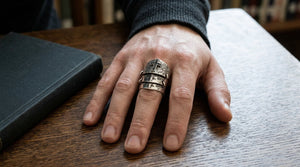 Linked silver armor ring with a black CZ cross worn on a relaxed hand beside a closed book