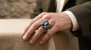A black-stone dragon claw ring worn with an olive coat and cream cuff at a linen-covered table.