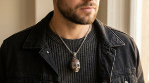 A copper-brain sugar skull pendant on a silver chain over charcoal knit and a black denim jacket.