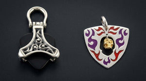 Celtic guitar pick holder with a black pick beside a silver pick-shaped pendant with colored motif and gold skull.