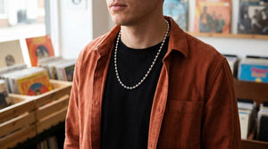 Adult wearing a silver ball chain over a black shirt and rust overshirt in a record shop.