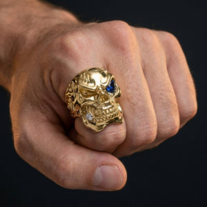 Solid 14k gold skull ring with sapphire eye and diamond tooth worn on hand for scale