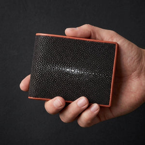 Man holding large black stingray leather bifold wallet with coral trim