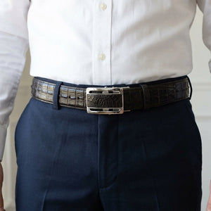 Ceinture en cuir de ventre et de queue de crocodile noir passée dans les passants d'un pantalon foncé