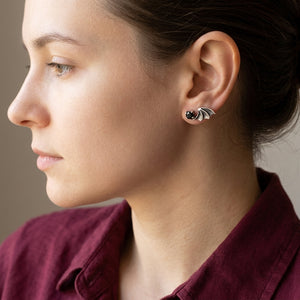 Un oxyde de zirconium noir et une aile de chauve-souris festonnée en argent reposent sur le lobe d'oreille d'un adulte au-dessus d'une chemise bordeaux.