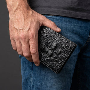 Cartera bifold de piel de cocodrilo hornback negra sostenida junto a la cadera