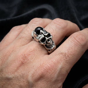 Серебряное кольцо с черепом и черным ониксом на руке оригинальной модели Bikerringshop на фоне черного бархата