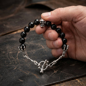 Black onyx and sterling silver skull bracelet held open in a natural hand above dark leather