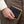 Black ostrich-leg bifold with broad scales and tan piping held beside brown trousers.