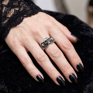 Anillo de plata compacto de calavera tribal con piedra negra puesto en una mano de mujer con uñas góticas negras