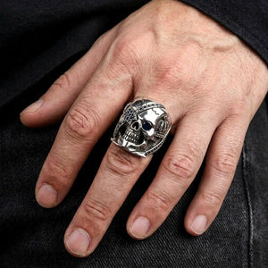 Blue sapphire pirate skull ring worn on a relaxed hand resting on dark denim