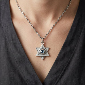 Blue acrylic-eye silver pendant styled on a silver chain above a charcoal shirt neckline; chain sold separately.