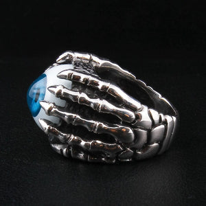 Anillo de plata esterlina con garra esquelética y ojo azul, toma de detalle en primer plano del anillo con ojo realista, centrada en las afiladas garras de plata