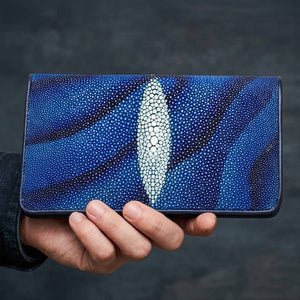 Cartera larga de cuero de raya bicolor azul sostenida en una mano, mostrando su panel central blanco