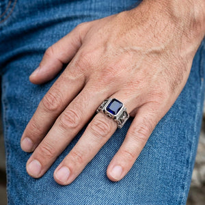 Kompakt rektangulär silverring med riddarsköld och blå sten buren på en avslappnad hand