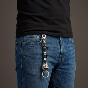 Silvernyckelring med dödskalle och flätat svart läder fäst i en bälteshälla av denim till en svart T-shirt