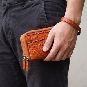 Cartera de piel de cocodrilo marrón con doble cremallera sostenida junto a la cadera