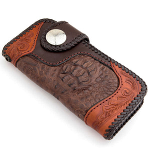 Closed crocodile wallet at an angle against white, showing the snap strap and carved leather ends.