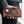 Brown crocodile and floral leather wallet held beside grey clothing, with the raised scales and snap strap facing forward.