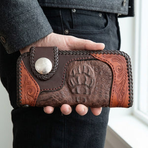 Brown crocodile and floral leather wallet held beside grey clothing, with the raised scales and snap strap facing forward.