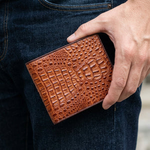 Cartera bifold de piel de cabeza de cocodrilo marrón sostenida junto a mezclilla oscura