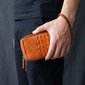 Cartera de piel de cocodrilo marrón claro con doble cremallera sostenida junto a la cadera