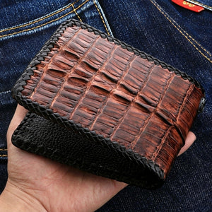 Brown crocodile bifold wallet supported in a hand, showing raised hornback scales and the black inner flap