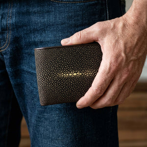 Cartera bifold de piel de raya marrón pulida sostenida junto a la cadera