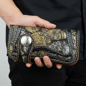 Portefeuille long en cuir noir à motif tête de mort et os sculptés tenu naturellement dans une main détendue