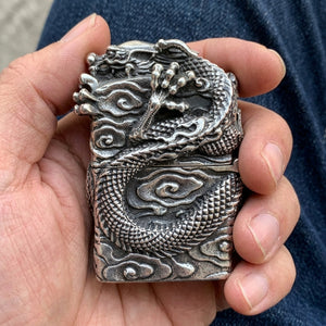 Chinese Dragon Sterling Silver Biker Lighter held in an adult hand above dark denim