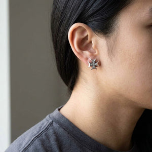 Un clou d'oreille en croix évasée en argent avec oxydes de zirconium transparents est porté près d'une oreille dégagée au-dessus d'une chemise anthracite.