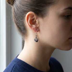 Une petite couronne en argent suspendue à un crochet d'oreille, présentée à côté d'une oreille dégagée et d'un haut bleu marine.