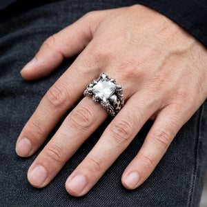 Clear stone dragon claw sterling silver ring worn on an adult hand resting on dark denim, showing the faceted center and sculpted silver shoulder.