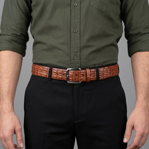 Cintura in coccodrillo a doppia cresta cognac allacciata su pantaloni neri sotto una camicia verde oliva.