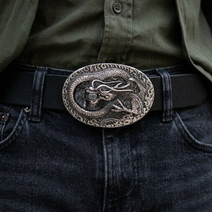 Hebilla ovalada de plata con dragón enrollado sobre un cinturón de estilo negro sobre vaqueros oscuros.