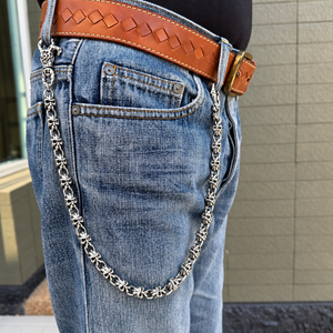 Cadena de plata para cartera con calaveras de demonio enganchada a unos vaqueros azules debajo de una camisa negra, mostrando sus eslabones de calavera