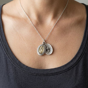 Guadalupe and sugar skull oval medals worn together on a silver chain above a charcoal scoop-neck shirt.