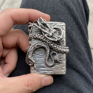 Dragon Book Sterling Silver Lighter held in an adult hand above dark denim