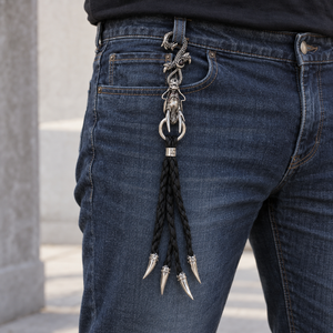 Nyckelring med silverdrake och svart flätat läder som hänger från en bälteshälla på jeans, med fyra ändar med silverspets