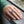 Der gravierte Krallenring umschließt einen Finger an einer Hand, die neben einer grünen Manschette auf Holz ruht.