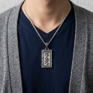 Ciondolo in argento con drago incorniciato su catena di presentazione sopra una maglia blu navy con scollo a V e cardigan grigio.