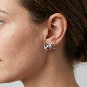 Galloping horse silver stud earring shown close-up on a woman’s ear