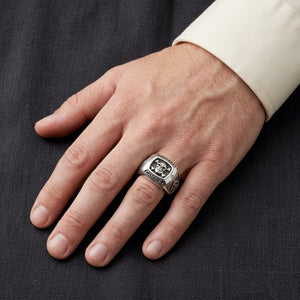 Gamble skull and crossbones silver signet ring worn on a hand over charcoal linen.
