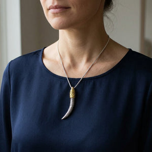 Ganesha slagtand-hanger van 925 sterling zilver met gouden detail, gestyled aan een zilveren ketting bij een donker overhemd