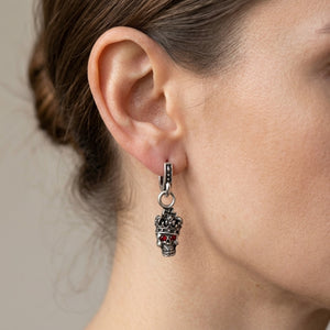 Pendientes colgantes de calavera con corona y granate en plata de ley 925 colgando de un aro articulado en una oreja de adulto