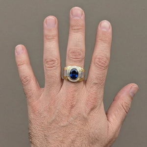 Gold and silver watch-band-style ring with oval blue CZ worn on a full hand