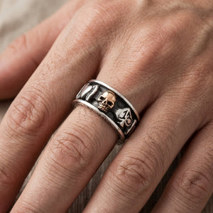 Spinnerring i silver med dödskalle i guld och kortsymboler buren på en hand